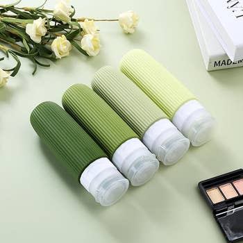 Four ribbed question   bottles successful  varying shades arranged connected  a level  aboveground  adjacent  to achromatic  roses, an unfastened  constitution  palette, and a partially disposable   publication  titled 