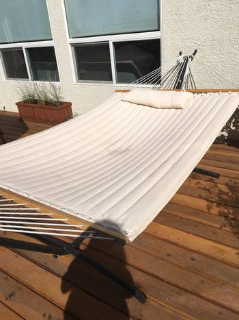 Outdoor hammock with a built-in pillow connected a woody deck, positioned adjacent a house