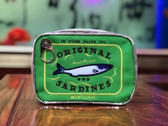 sardine can-shaped bag on a wooden surface, with a fish illustration and the text 