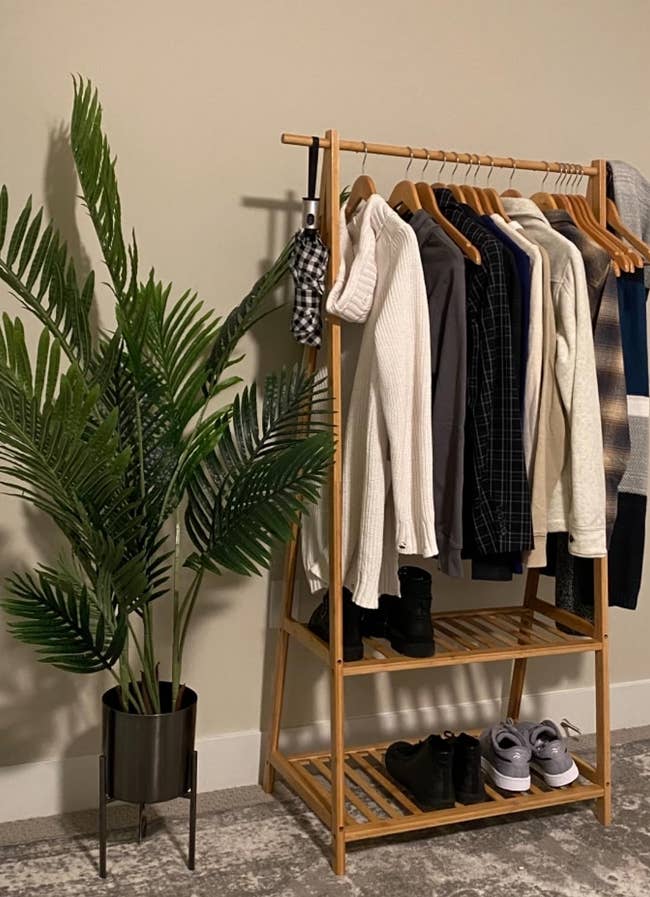 reviewer's bamboo garment rack holding shoes on bottom two shleecs with clothes hanging on the top
