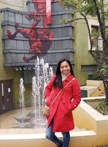 another reviewer wearing red peacoat in front of fountain