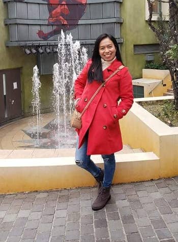 reviewer wearing red peacoat in front of fountain