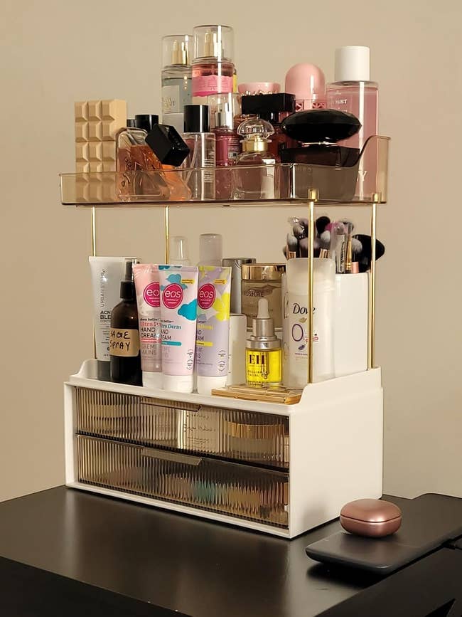 Makeup organizer on a table with skincare and beauty products neatly displayed on two tiers, alongside a closed compact case. Perfect for vanity storage