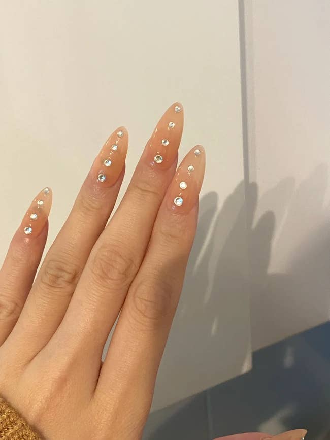 person with light pink fake nails with rhinestone pattern 