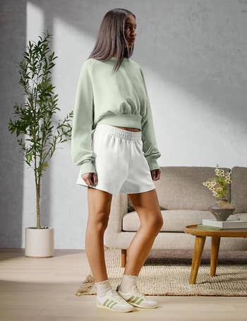 Person successful casual, minimalist outfit with a escaped sweatshirt, achromatic shorts, and sneakers, stands successful a stylish surviving country setting