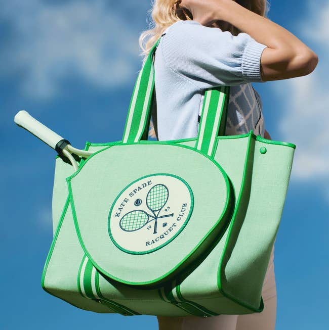 model holding the green square tote bag with racket-shaped pocket on the outside with a tennis racket in it