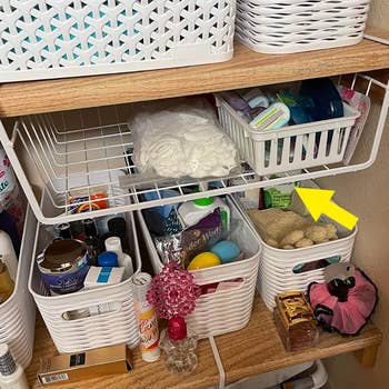 reviewer's white under-shelf basket hanging in the bathroom holding toiletries
