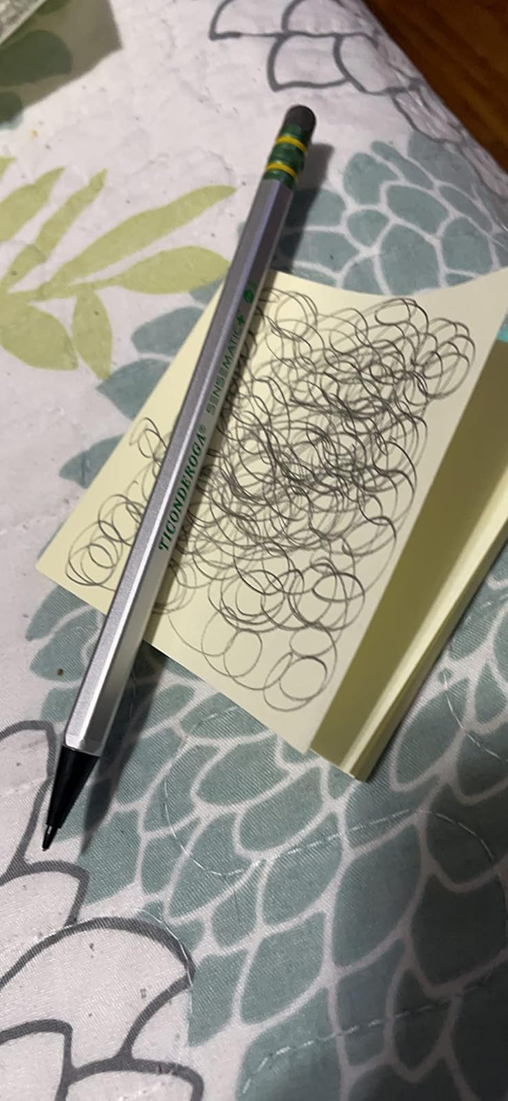 Sebuah pena diletakkan di atas buku catatan dengan coretan acak di atasnya, bertumpu pada permukaan yang berpola