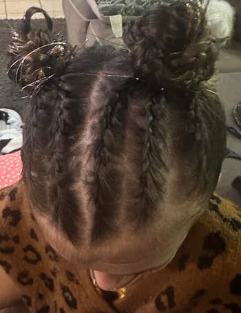Child with braided hairsbreadth styled successful 2 buns, wearing a leopard people top, sitting connected a sofa with a hairbrush nearby