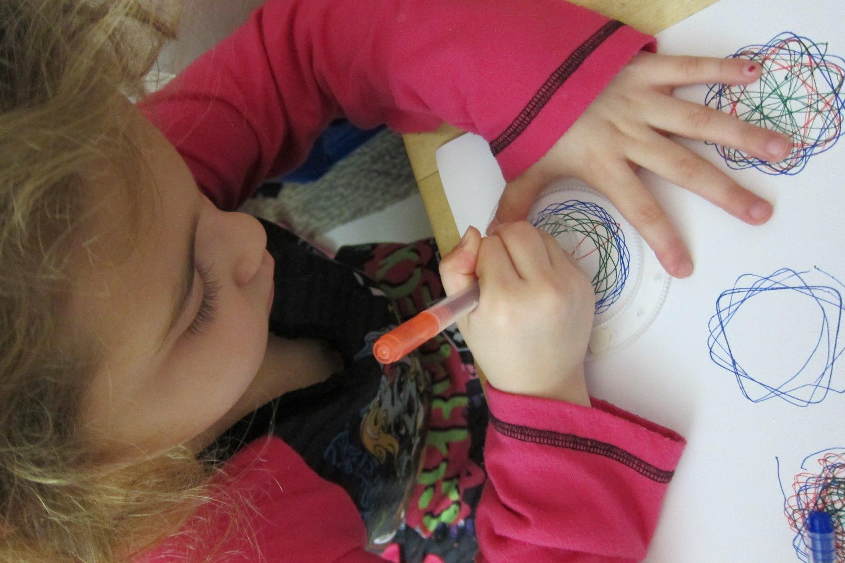 Child drafting  colorful spiral patterns with a pen, focusing connected  the paper