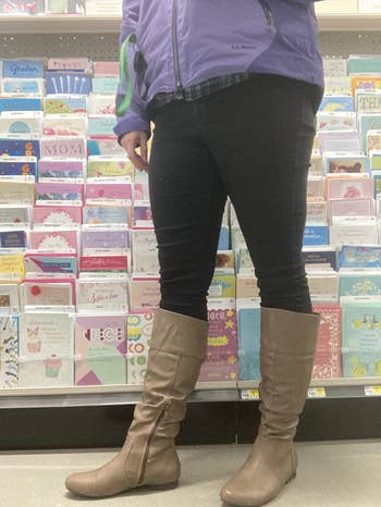 Person buying  for greeting cards, wearing a jacket, jeans, and knee-high boots successful  a store   aisle