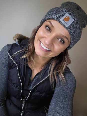 Person smiling in a cozy outfit, wearing a gray beanie and a black puffer vest, suitable for winter fashion