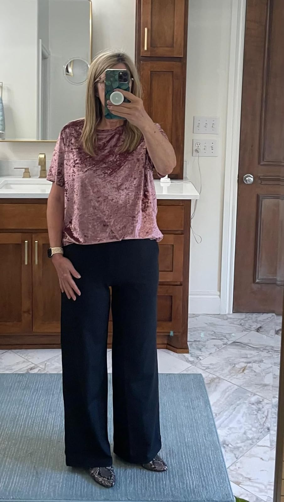 A person takes a mirror selfie wearing a velvet top and wide-leg pants in a bathroom
