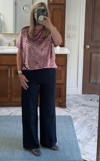 A person takes a mirror selfie wearing a velvet top and wide-leg pants in a bathroom