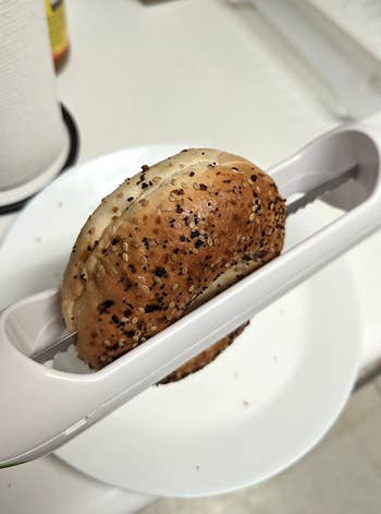 A bagel being sliced with a bagel slicer on a white plate
