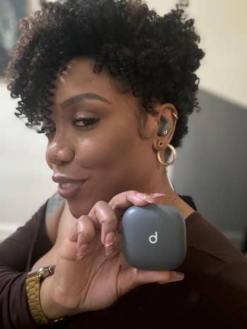 Person smiling while holding wireless earbuds case.