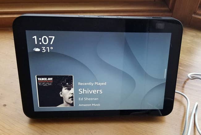 A reviewer's device on a table with the time, temperature and music playing on the display