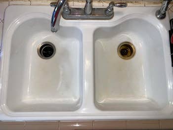 Dual-basin room  descend  with modern   faucets; 1  drain has a noticeable discoloration