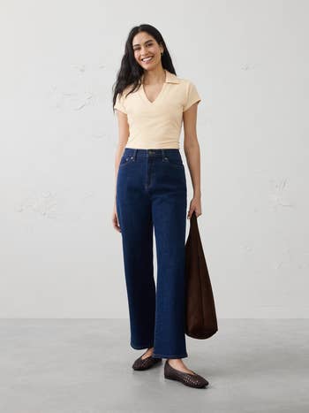 Woman successful  casual outfit with a short-sleeve apical  and wide-leg jeans, holding a tote bag, lasting  successful  a minimalist setting