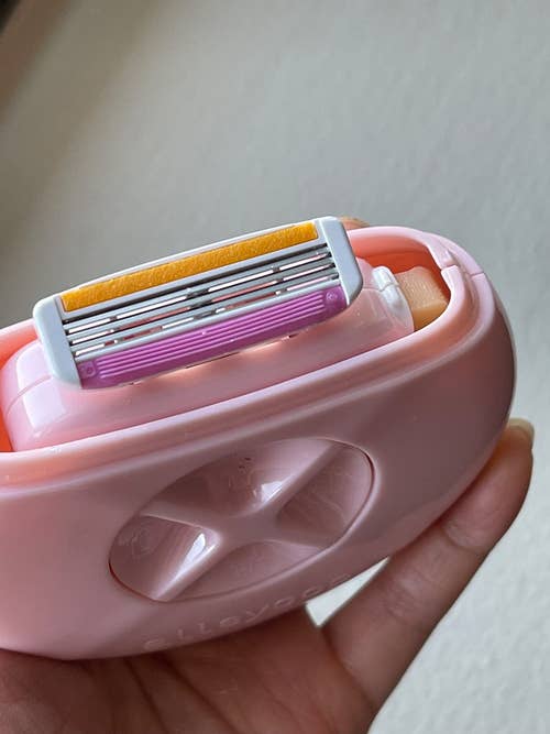 reviewer holding the pink circular travel shaver, showing the razor head it comes with