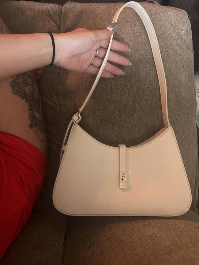 Person holding a chic, cream shoulder bag with a gold clasp, resting on a couch
