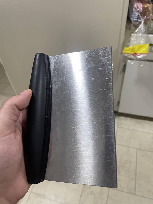 Metal seat scraper held successful hand, featuring a achromatic grip and a stainless alloy leaf with measurement markings