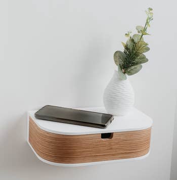 A floating shelf with a vase holding greenery and a smartphone on it, suggesting minimalist decor shopping