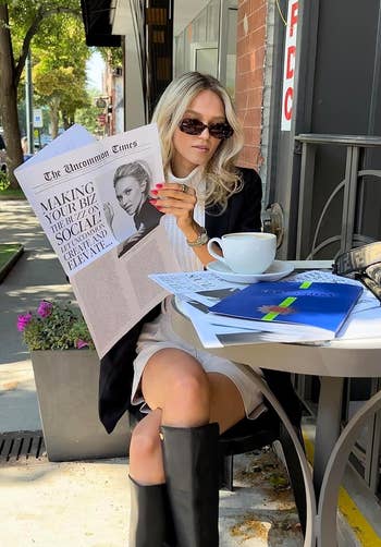 reviewer in stylish black jacket and sunglasses reads a newspaper titled 