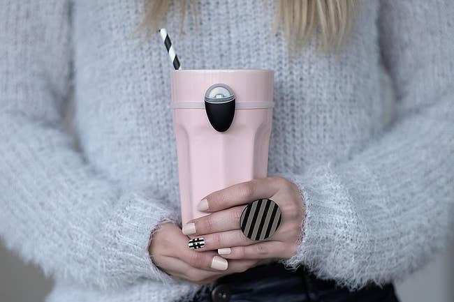 Person holding a pink tumbler with a small black hydration reminder tool attached to it