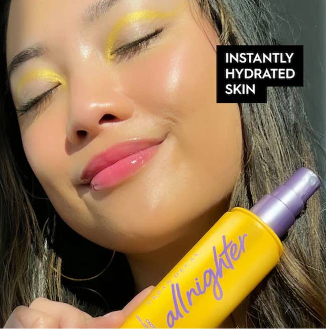 Model with vibrant makeup posing with bottle of setting spray 