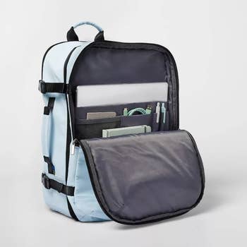 An open light blue and gray backpack with compartments showing books and pens, suitable for shopping