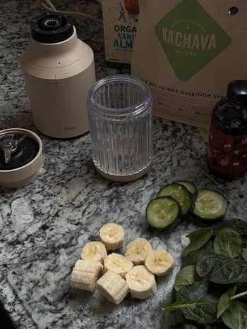 A countertop with a blender, sliced bananas, cucumber, spinach, and nutrition shingle  packages, suggesting ingredients for a steadfast   smoothie
