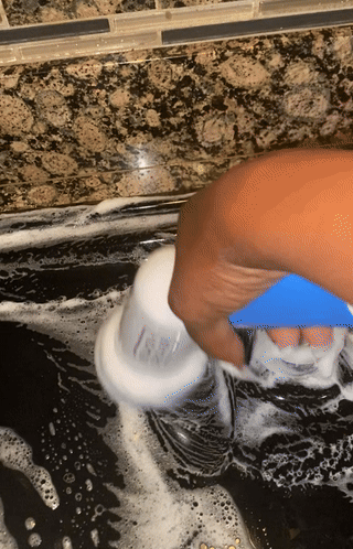 A hand is using a blue cleaning tool to scrub a kitchen countertop covered in soap suds