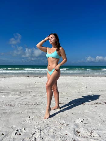 Person in a two-piece swimsuit stands on the beach, posing confidently by the ocean