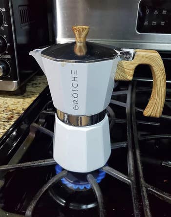 White moka pot with wooden handle making espresso on a lit stove 