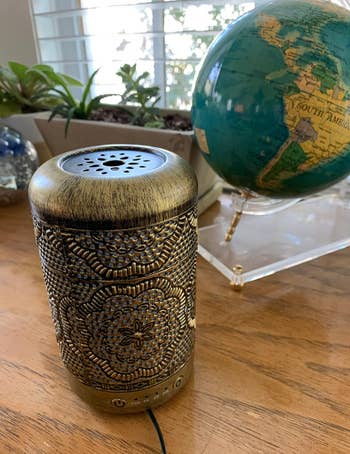 reviewer's gold metal vintage diffuser on a desk next to a globe