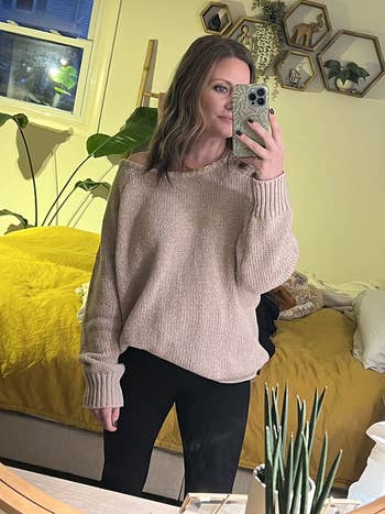 A pistillate takes a reflector selfie successful a cozy sweater and leggings, lasting successful a stylishly decorated chamber with plants and partition shelves