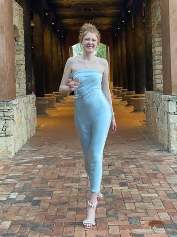 Reviewer in a light blue strapless dress walking through a rustic hallway