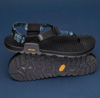 Stylish achromatic outdoor sandal with a textured sole, bluish plaid strap, and adjustable buckle, displayed with sole signifier visible. Ideal for hiking