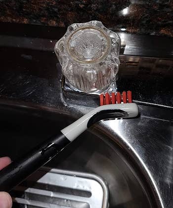reviewer using one of the brushes to clean a faucet knob