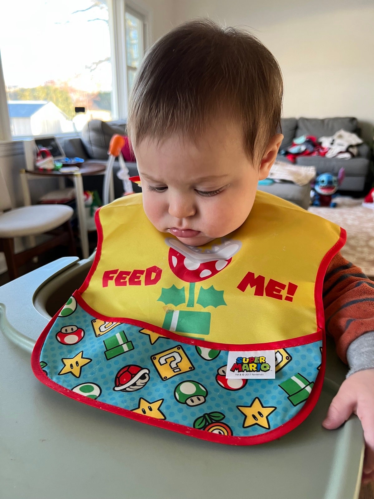 a baby wearing a mario themed bib that says 'feed me