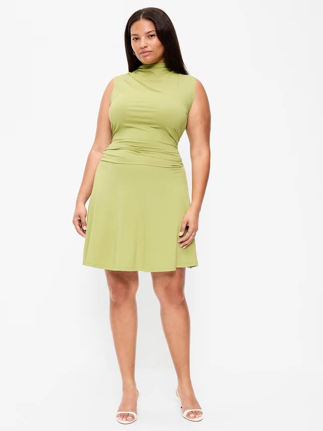A idiosyncratic is wearing a sleeveless, knee-length formal with a precocious neckline and subtle ruching, paired with open-toe heels