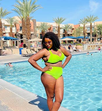 Person in neon green swimwear with sunglasses by a poolside, hand on hip, clear skies in the background