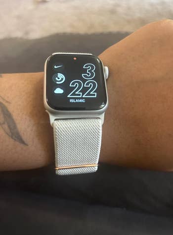 Close-up of a smartwatch connected  a person's wrist showing the clip  and weather, with a stylish light-colored band