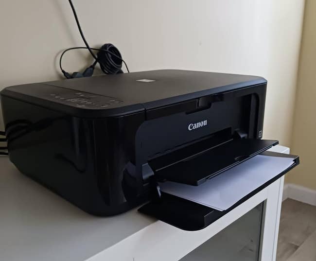 Canon printer on a white cabinet against a light wall, showcasing a sleek design for home office needs
