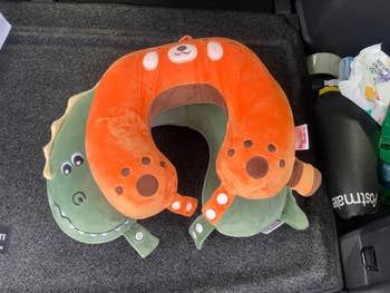 Plush cervix  pillow with a playful carnivore  plan  connected  1  broadside  and a dinosaur connected  the other, placed successful  a car