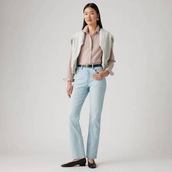 Model wearing a striped shirt, light-wash jeans, and flats, with a airy  sweater draped implicit    shoulders