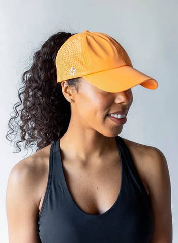 Model in a orange baseball cap with a high ponytail coming out of the back  