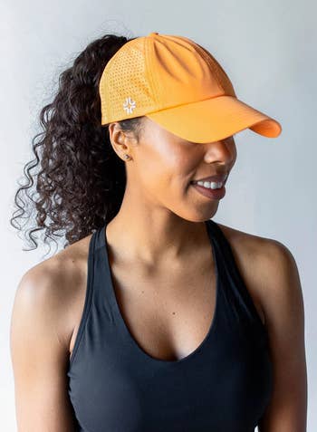Model in a orange baseball cap with a high ponytail coming out of the back  
