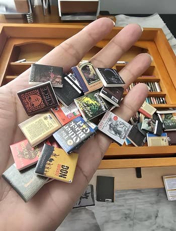 A manus  holds miniature publication  covers, showcasing a scope  of fashionable  titles, with a drawer afloat  of tiny  books successful  the background